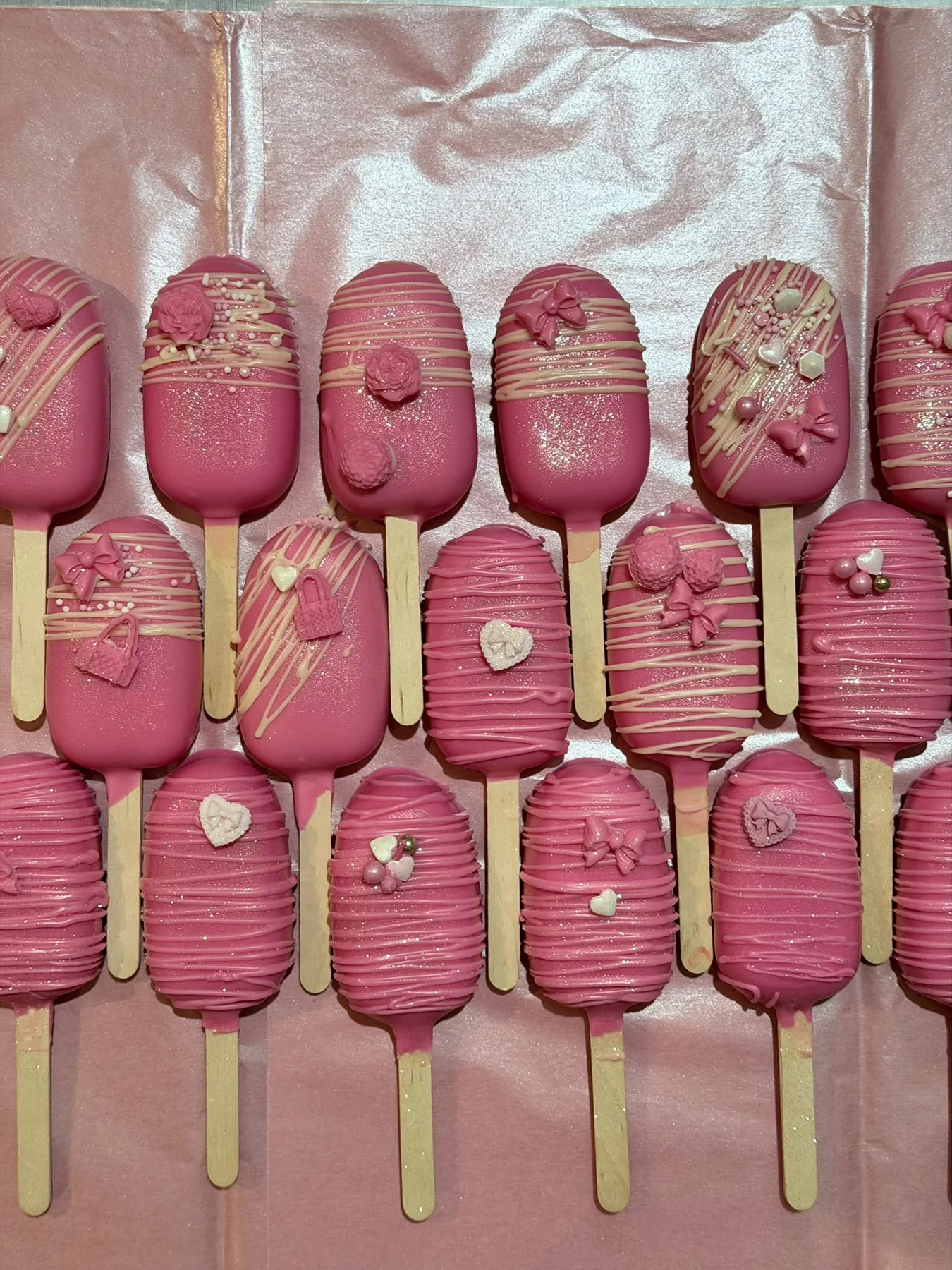 Pink chocolate cakesicles with decorative sprinkles and drizzles.